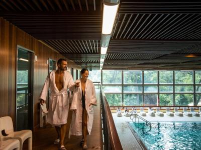 Paar im Bademantel geht an einem Hallenbad vorbei.