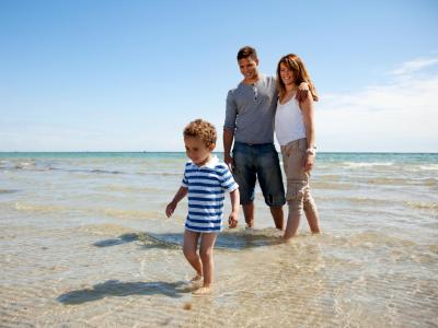 Famiglia che cammina in riva al mare in una giornata di sole.