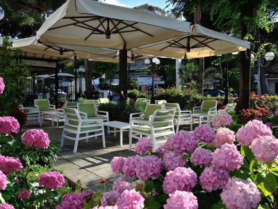Giardino con sedie bianche, ombrelloni e fiori rosa.