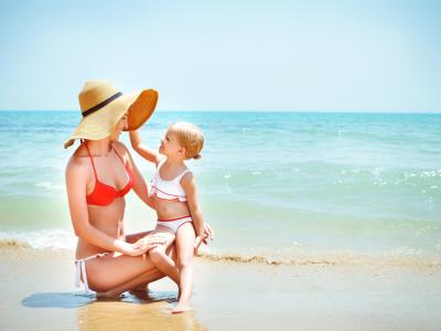 Mamma e figlia sorridenti giocano felici sulla spiaggia soleggiata.