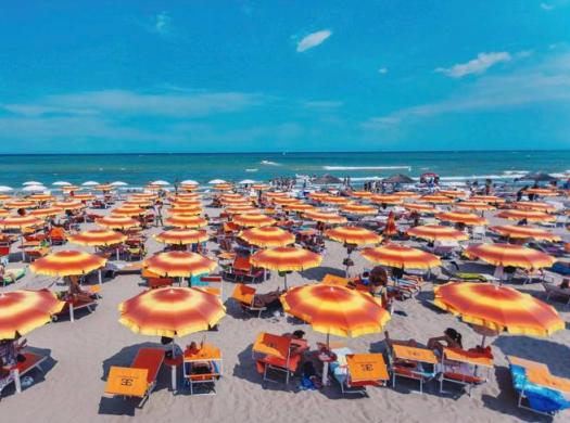 Spiaggia affollata con ombrelloni arancioni e mare calmo.