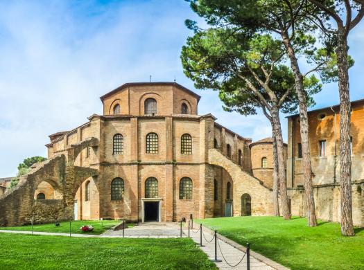 Antico edificio in mattoni con giardino, scale esterne e alberi.