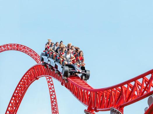Persone su montagne russe rosse in un parco divertimenti.