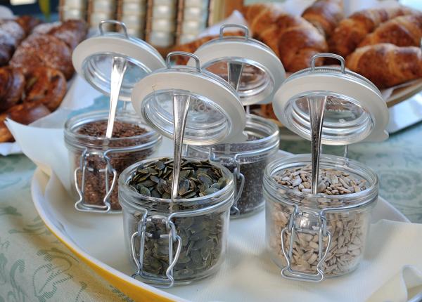 Jars of various seeds with croissants in the background.