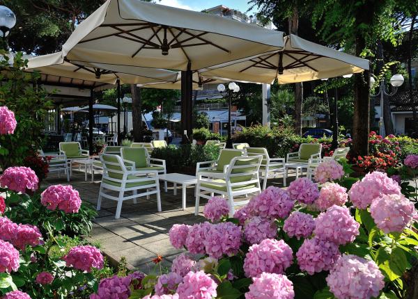 Giardino con sedie bianche, ombrelloni e fiori rosa.
