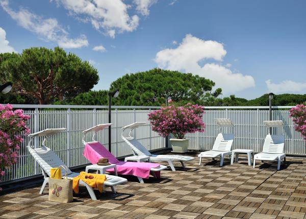 Terrazza con lettini, fiori rosa e cielo blu.