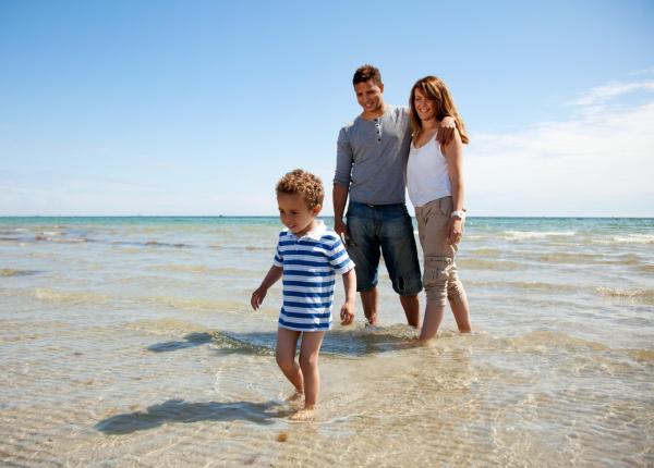 Famiglia che cammina in riva al mare in una giornata di sole.