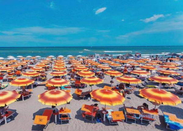 Spiaggia affollata con ombrelloni arancioni e mare calmo.