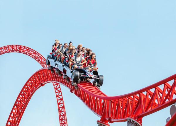 Persone su montagne russe rosse in un parco divertimenti.