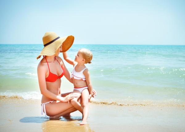 Mamma e figlia sorridenti giocano felici sulla spiaggia soleggiata.